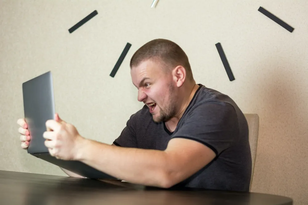 A guy holding a laptop up yelling at it